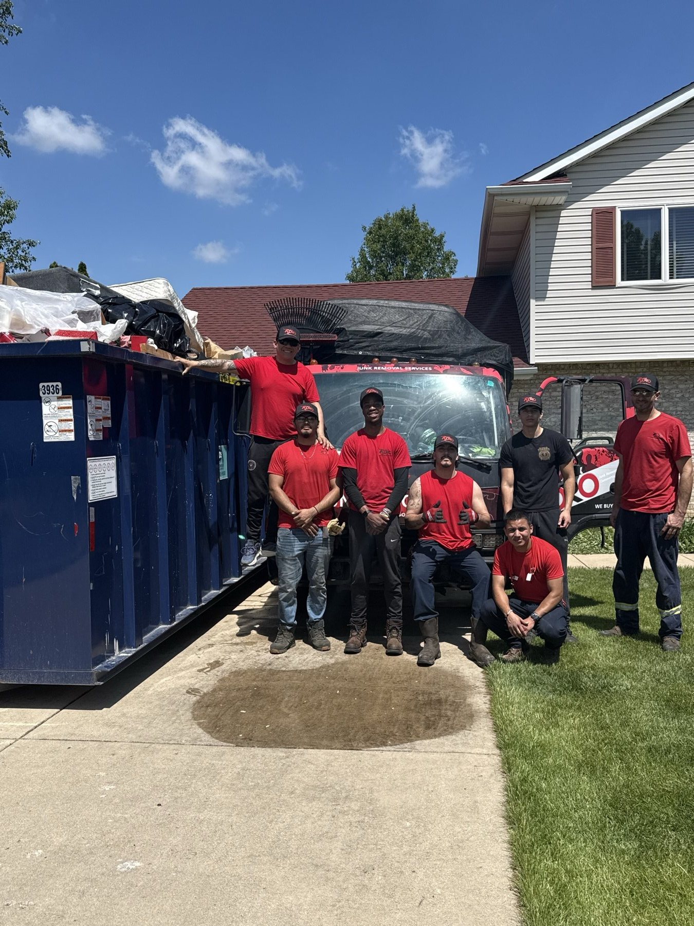 The full Junk Toro crew in red shirts in front of their truck and loaded dumpster